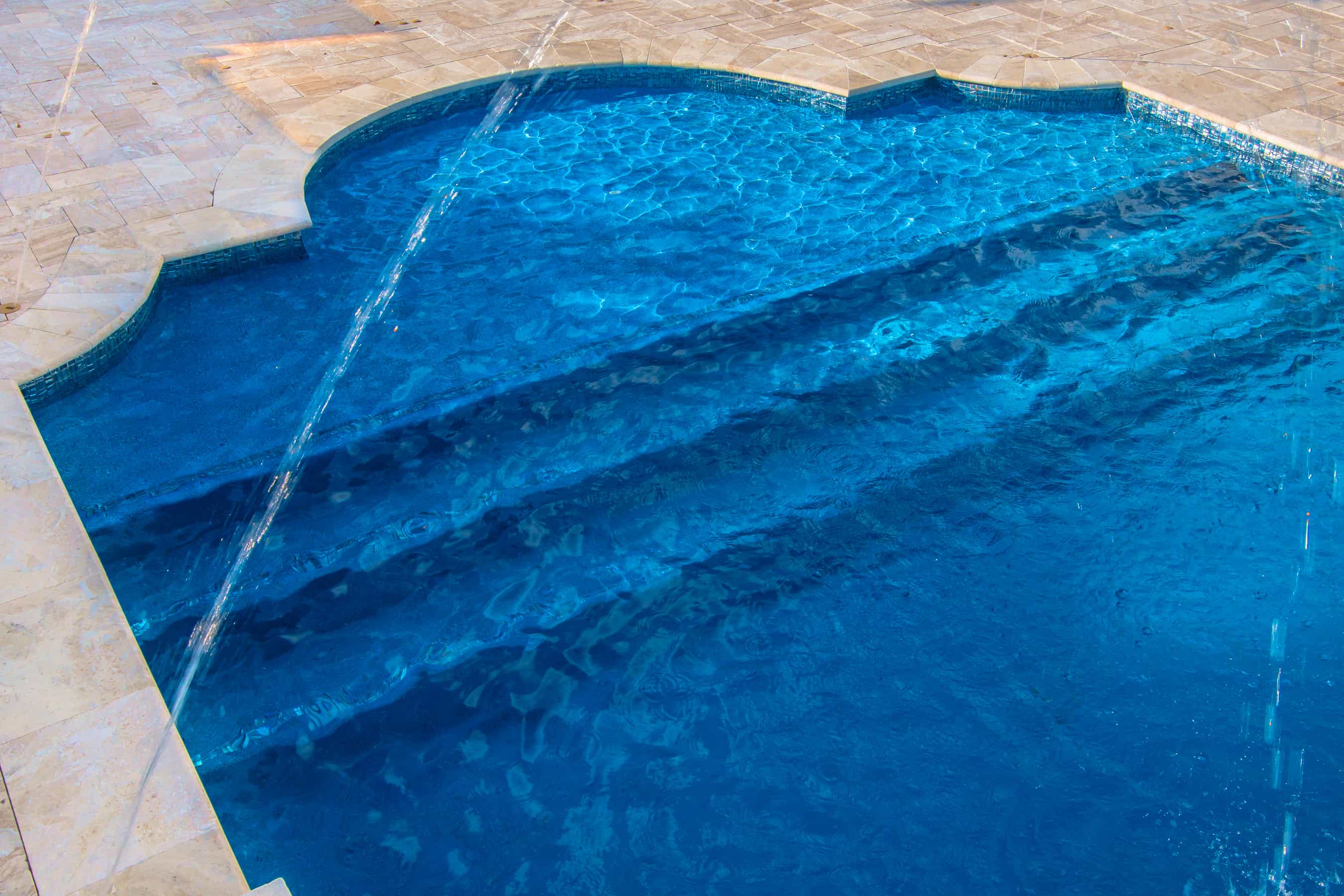 Close up of bright blue pool in the backyard of a home. Water spraying over pool.