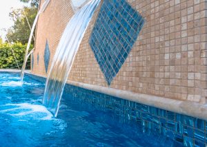 Luxury bright blue pool with beautiful tiles. Waterfall pouring water.